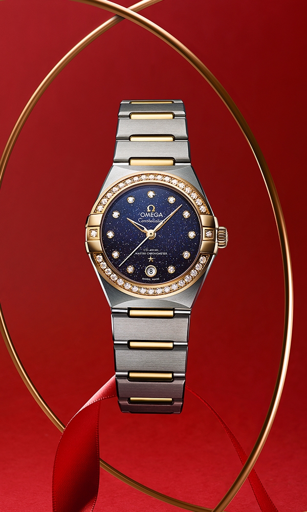 這款29毫⁠米腕錶以18K黃金及不銹鋼鑄造⁠，錶圈鋪鑲鑽石⁠，襯上藍色砂金玻璃錶面⁠，鑲飾鑽石小時刻度⁠，6時位置設有日曆窗⁠。指針⁠、Omega標誌⁠、星座星徽和鑽石座同樣以18K黃金鑄造⁠。這款腕錶配置Omega Co-Axial Master Chronometer機芯8700，通透⁠⁠的弧拱造形防磨損藍寶石水晶錶背可⁠⁠一覽機芯⁠⁠的造形態⁠⁠。